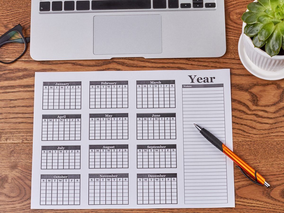 Printed year planner and pen beside a laptop on a wooden desk